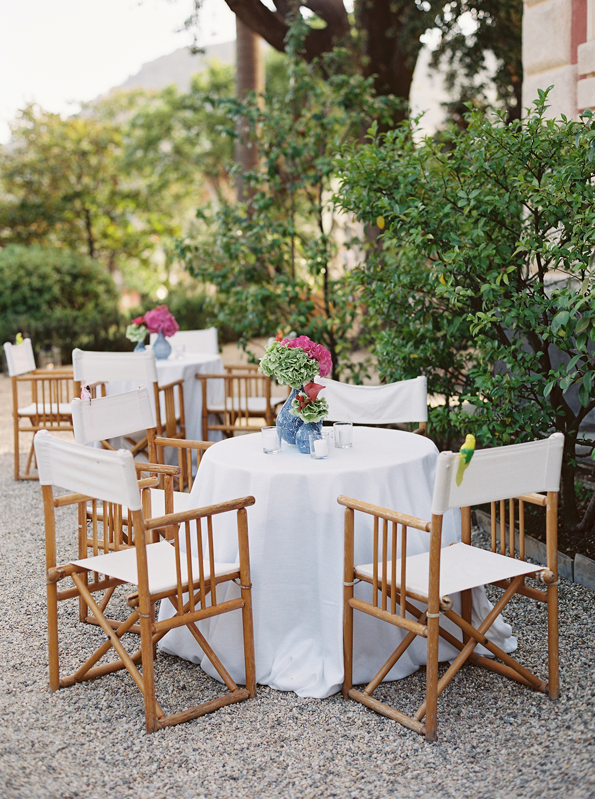 Outdoor cocktail tables set in the gardens of Villa Durazzo with wooden chairs and floral centerpieces