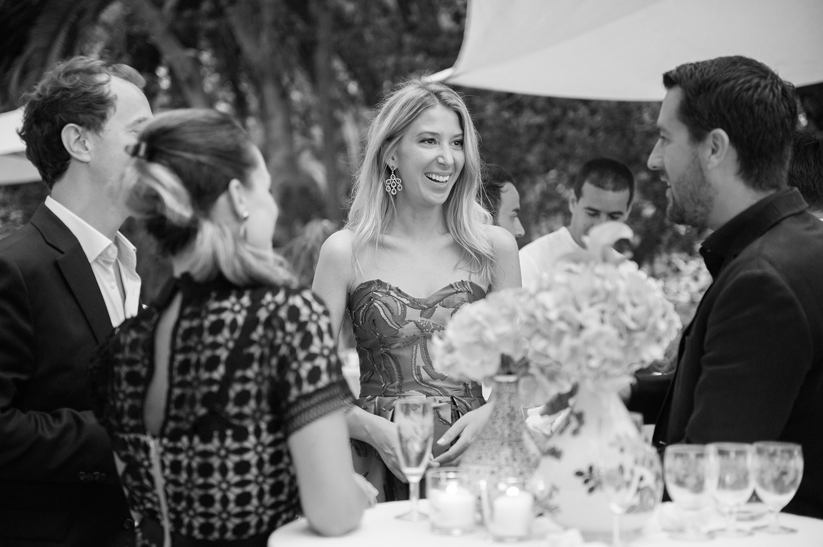 Black and white photo of wedding guests laughing and talking around a cocktail table during the reception