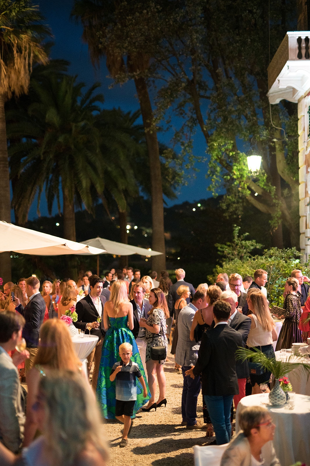 Nighttime wedding reception with guests socializing outdoors under palm trees and soft lighting