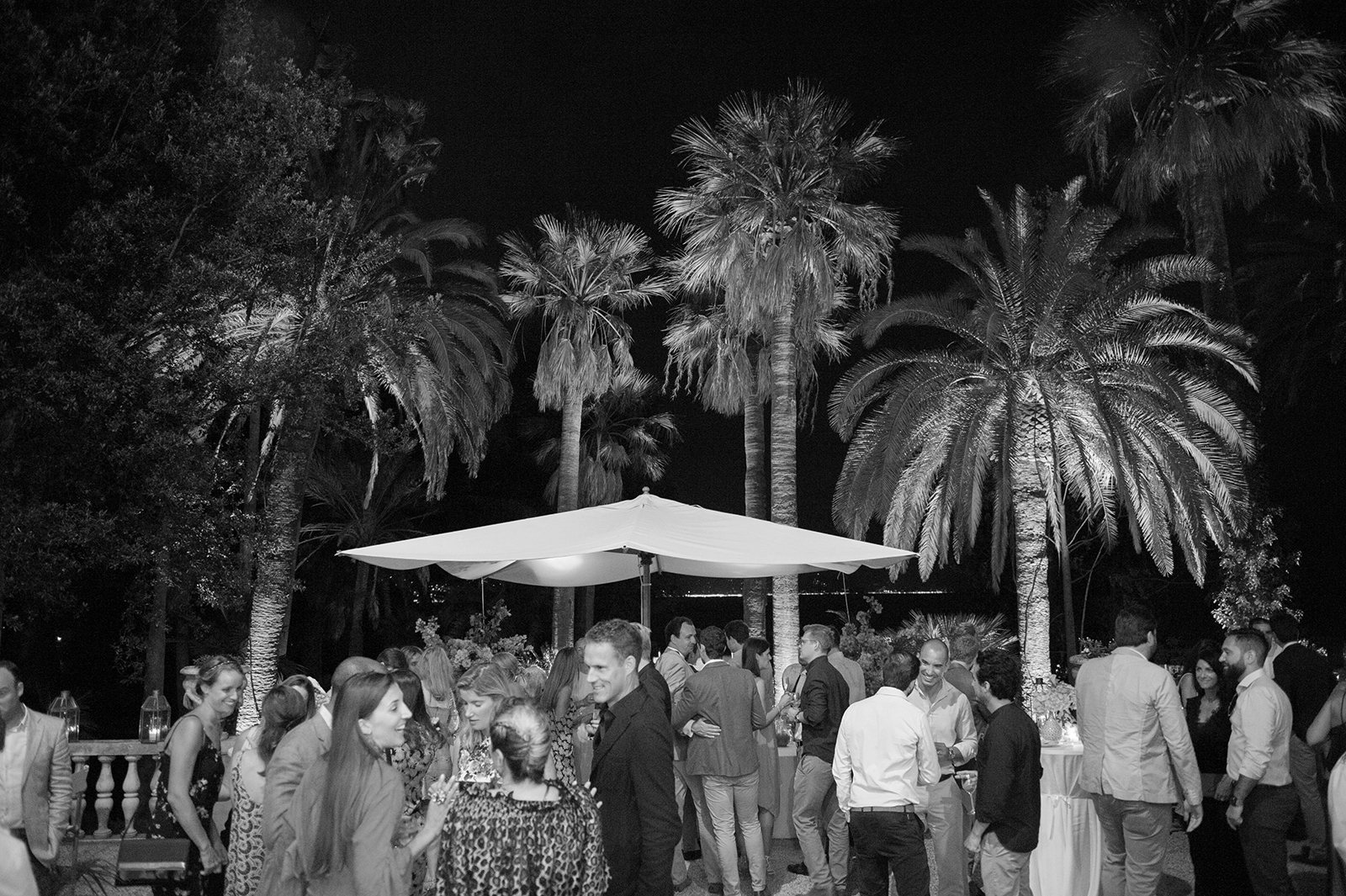 Lively outdoor wedding reception at night with guests dancing and mingling beneath palm trees