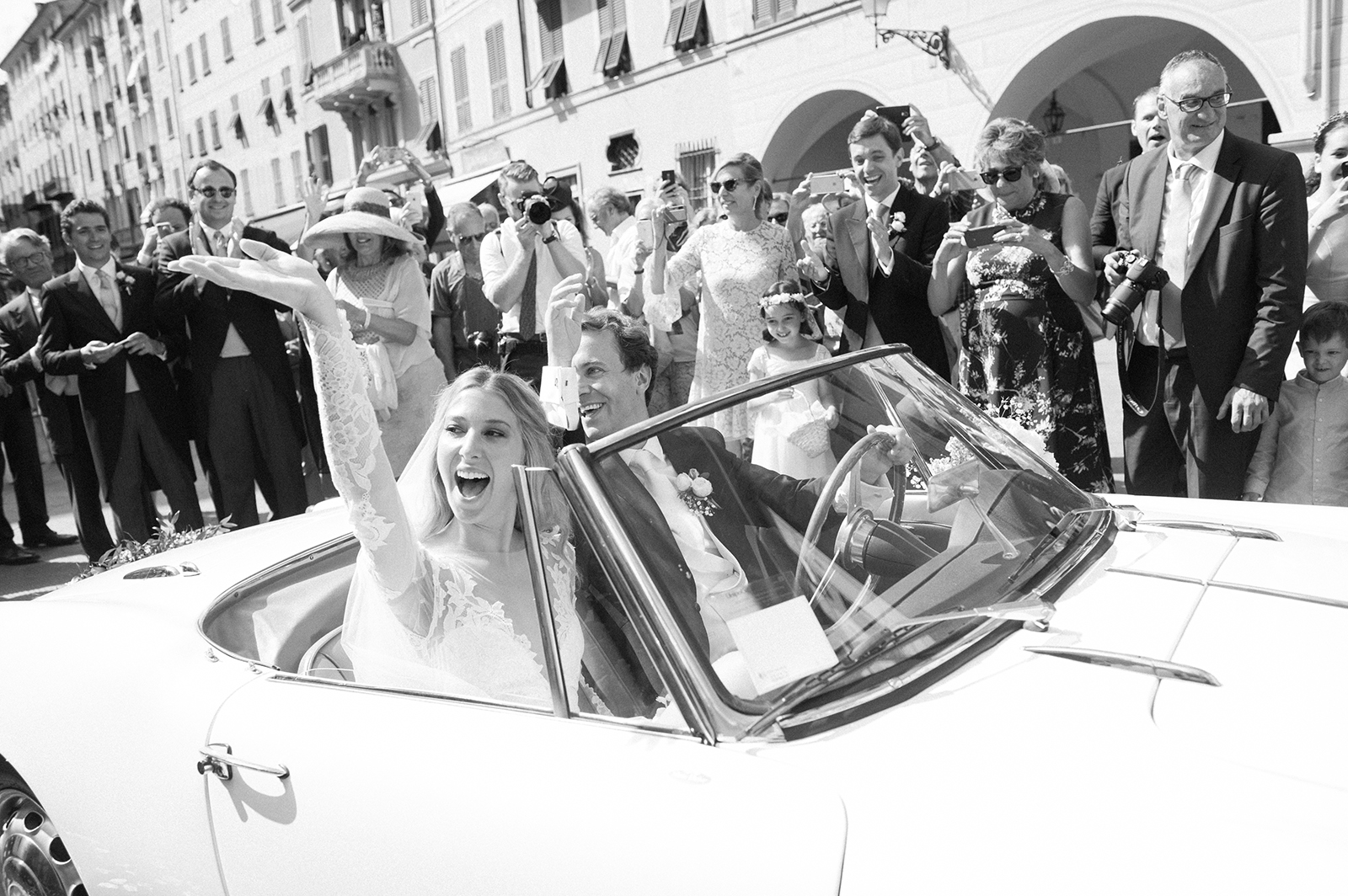 Bride waving to guests from vintage wedding car in Portofino