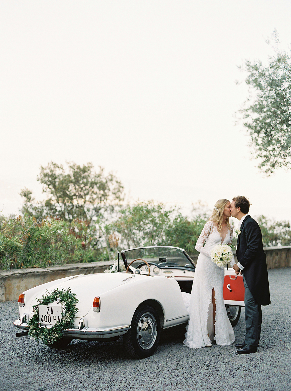 Bride and groom kissing beside vintage car at La Cervara Abbey wedding in Portofino, Italy