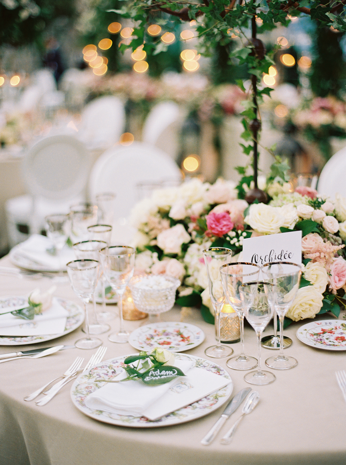 Romantic wedding table setting with pastel florals, fine china, crystal glassware, and soft candlelight