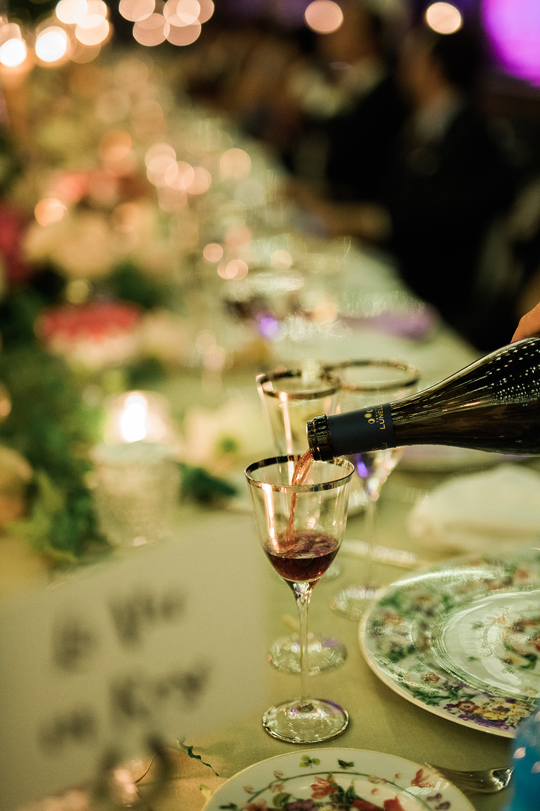 Close-up of red wine being poured into a glass during an elegant candlelit wedding dinner