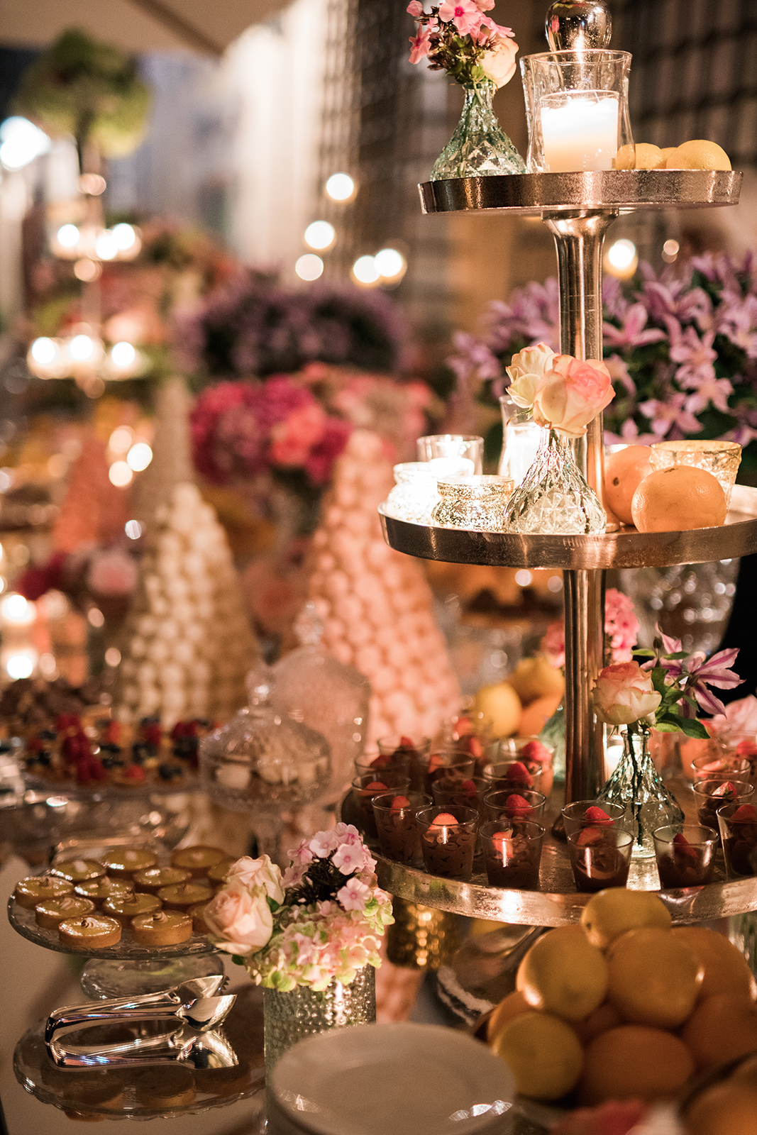 Elegant dessert display with candles, florals, and pastel sweets arranged for a luxury wedding reception