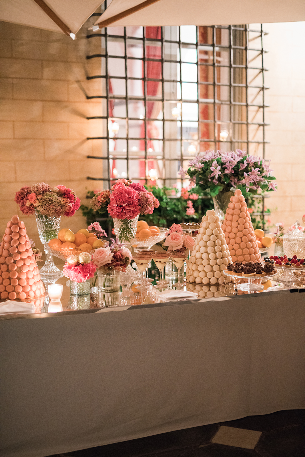 Wedding dessert table featuring macarons, floral arrangements, and soft candlelight in an outdoor setting