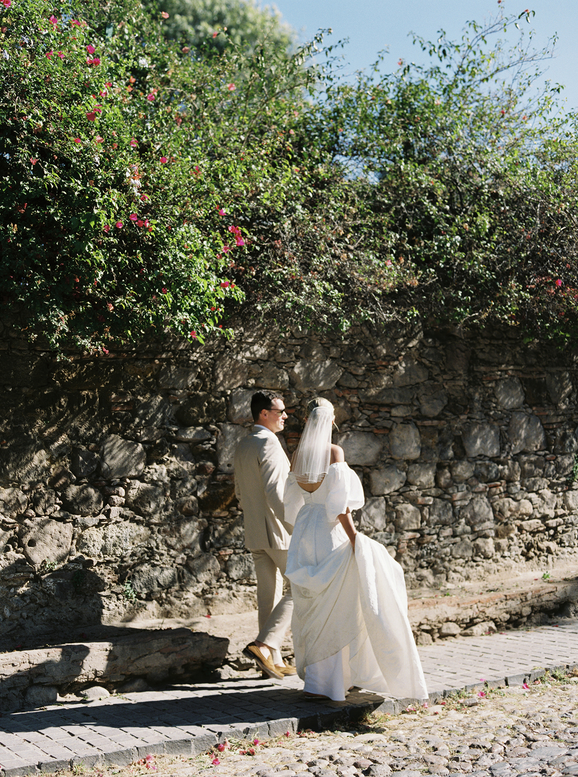 Wedding couple walking together along stone wall in San Miguel de Allende