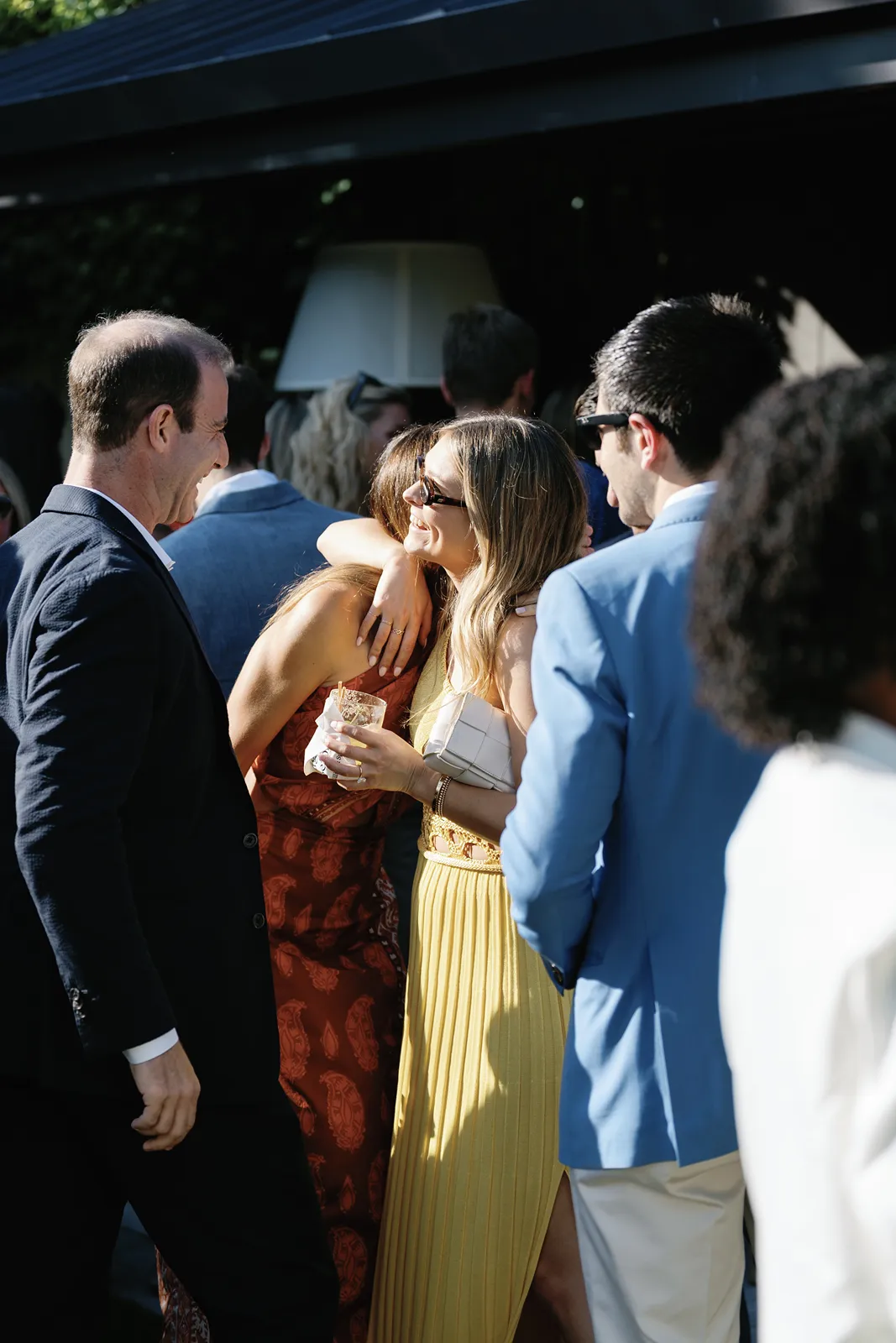 Guests greeting one another with hugs and drinks during a rehearsal dinner