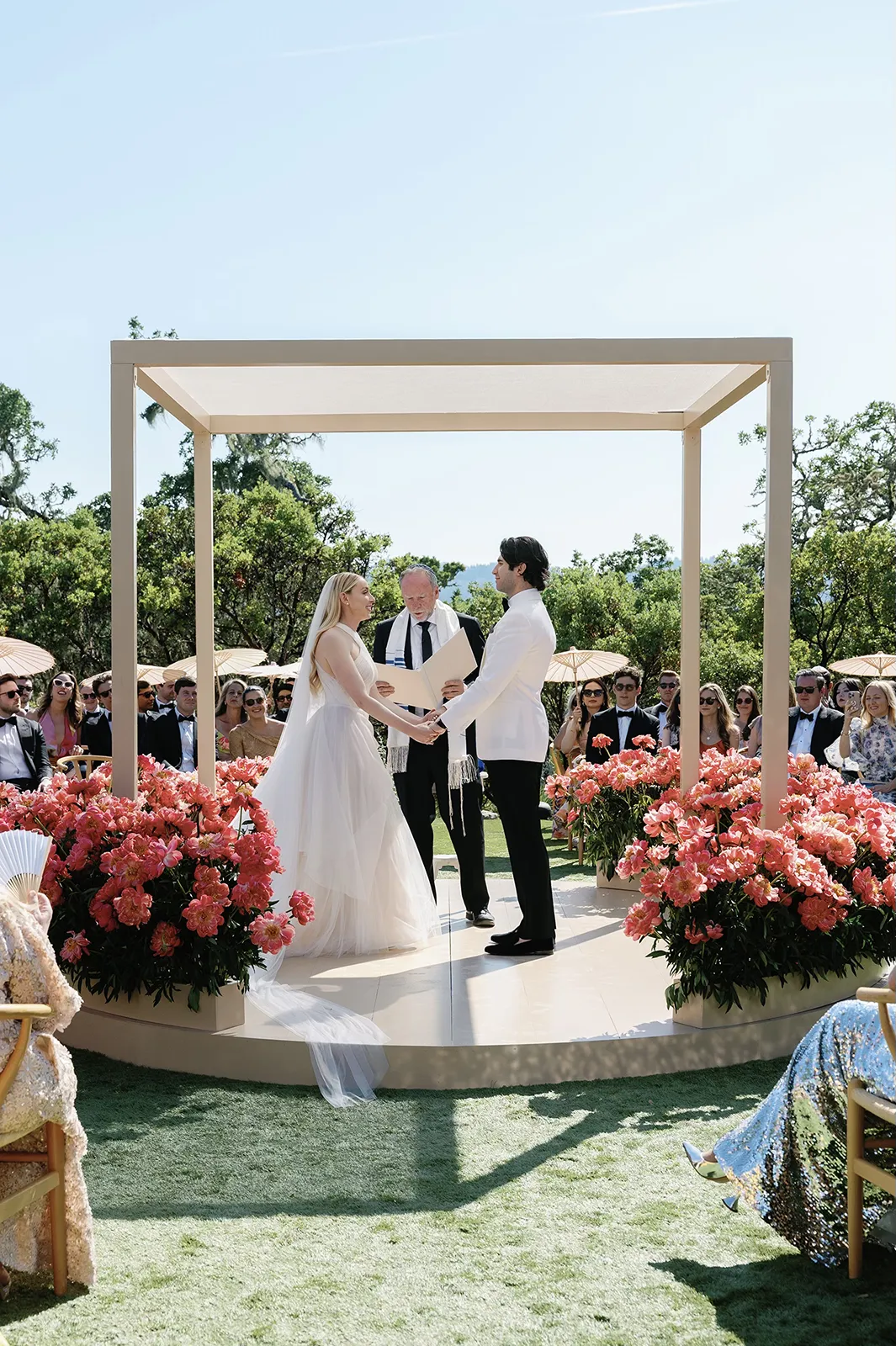 Bride and groom exchanging vows beneath a modern chuppah surrounded by pink floral arrangements at Montage Healdsburg