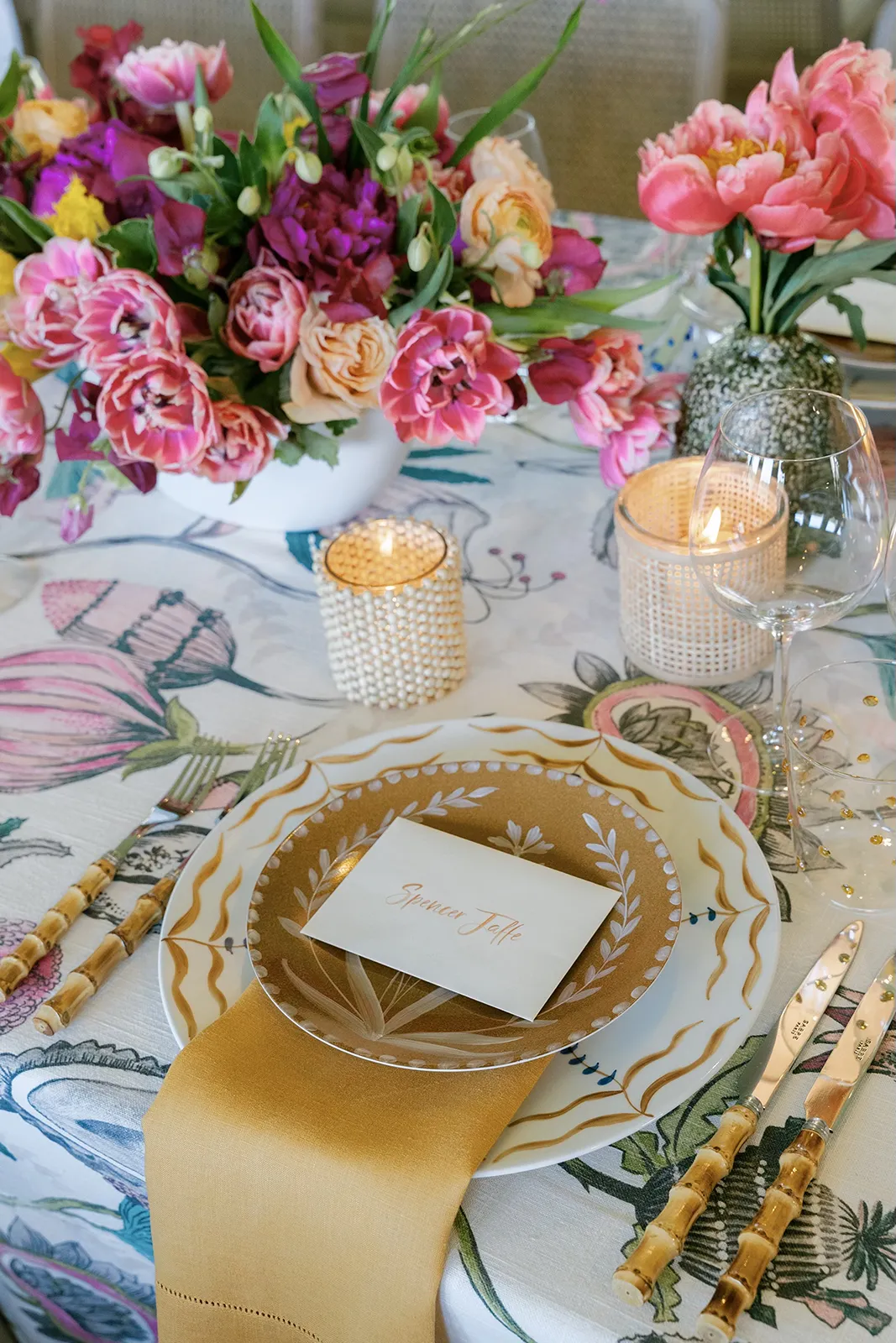 Wedding table setting with colorful floral centerpiece, gold-rimmed plates, bamboo flatware, and candlelight