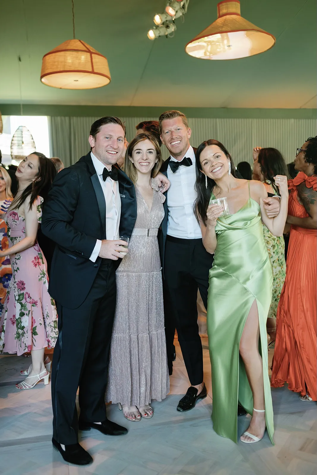 Wedding guests smiling and dancing together indoors during the reception beneath woven pendant lights
