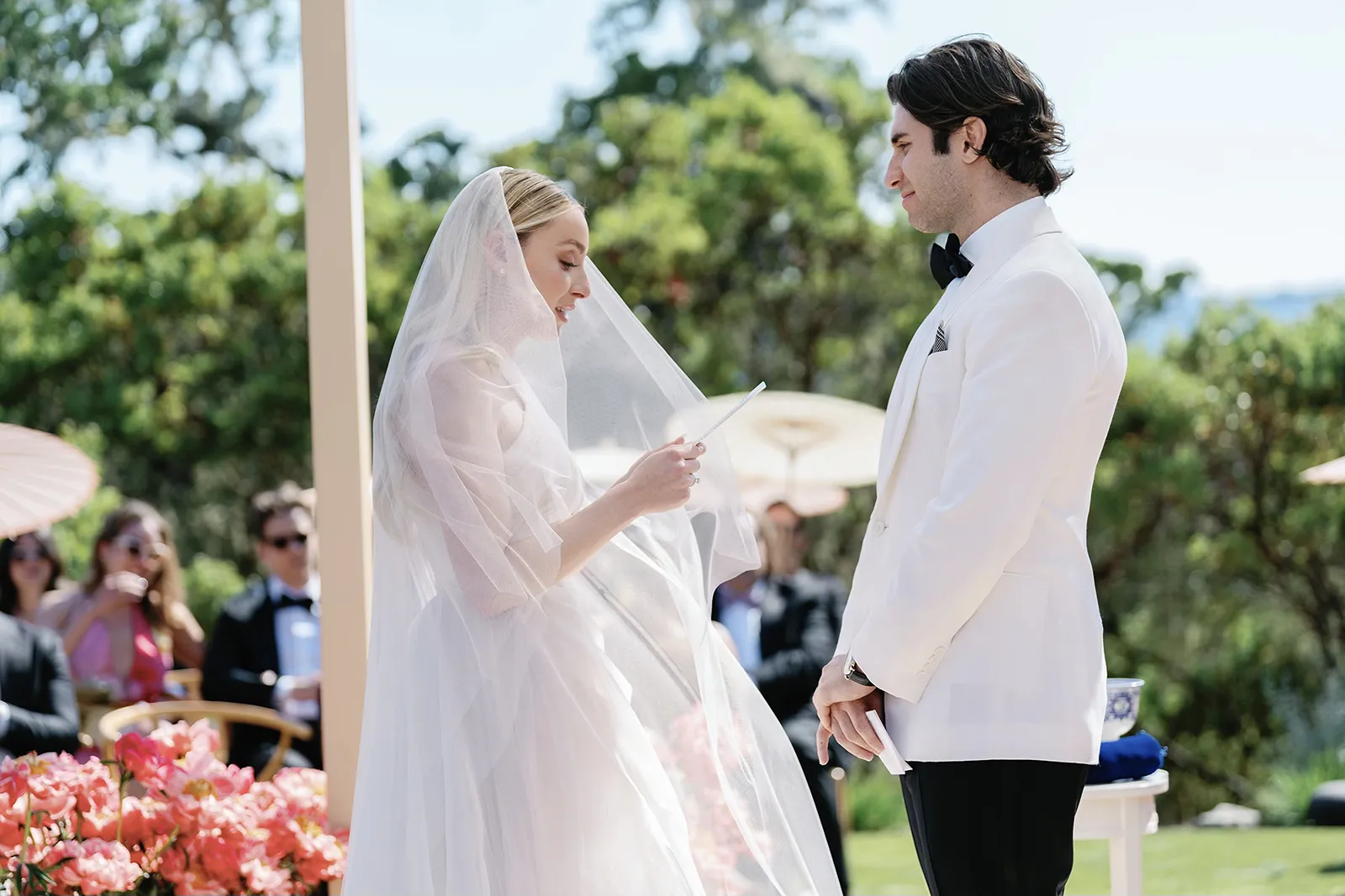 Bride reading her vows to the groom during an outdoor wedding ceremony with guests seated behind them