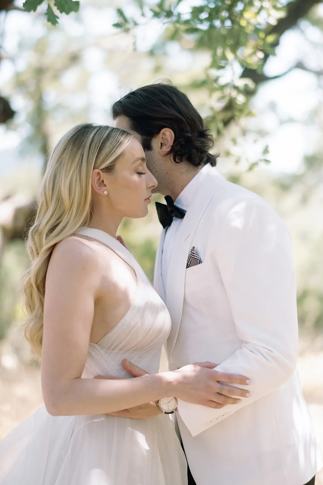 Bride and groom embracing closely beneath trees during an intimate wedding portrait