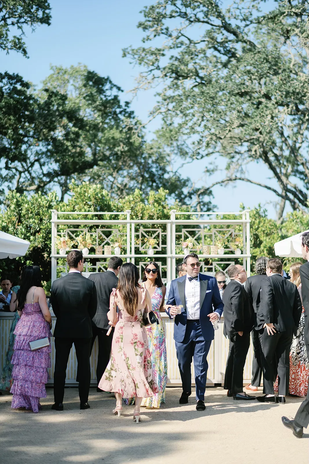 Wedding guests mingling and enjoying drinks during an outdoor cocktail hour surrounded by oak trees