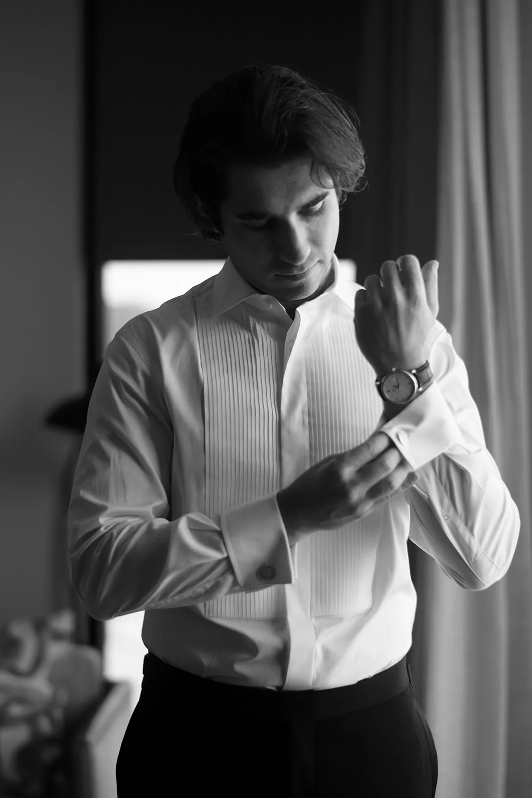 Black-and-white photo of the groom adjusting his cufflinks while getting ready