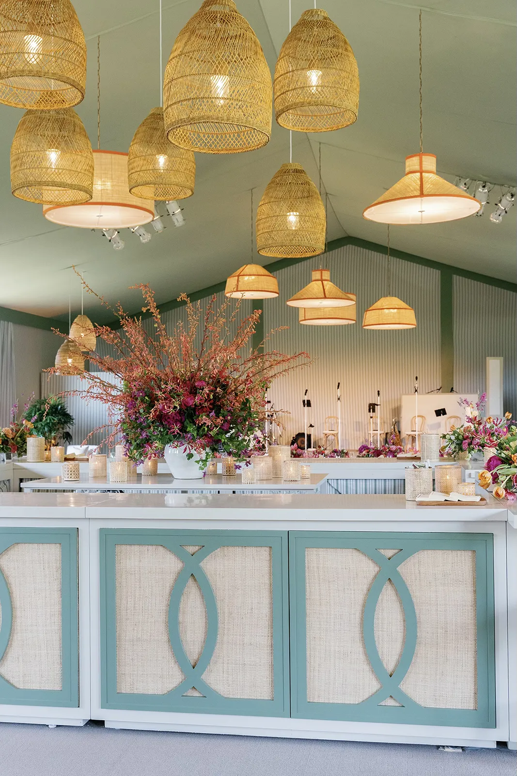 Elegant wedding reception bar at Montage Healdsburg featuring soft green cabinetry, candlelight, and a large floral arrangement beneath woven pendant lights