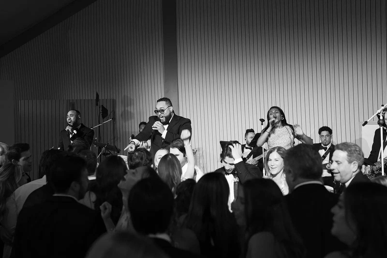 Black-and-white image of a live band performing on stage as wedding guests dance and raise their hands during the reception at Montage Healdsburg