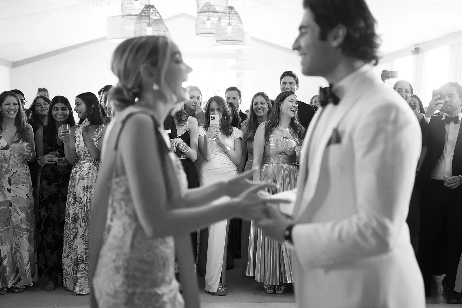 Bride and groom holding hands during their first dance at a wedding reception surrounded by guests