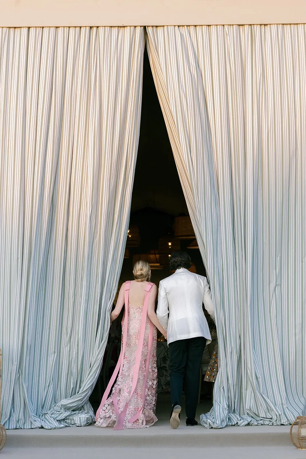 Bride and groom holding hands as they walk through tall draped curtains into their wedding reception