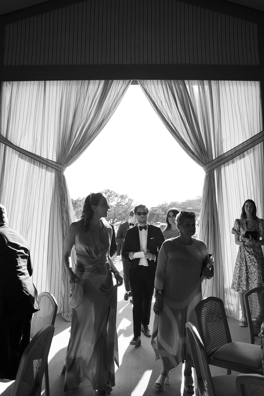 Wedding guests walking into the reception space through tall open curtains filled with natural light