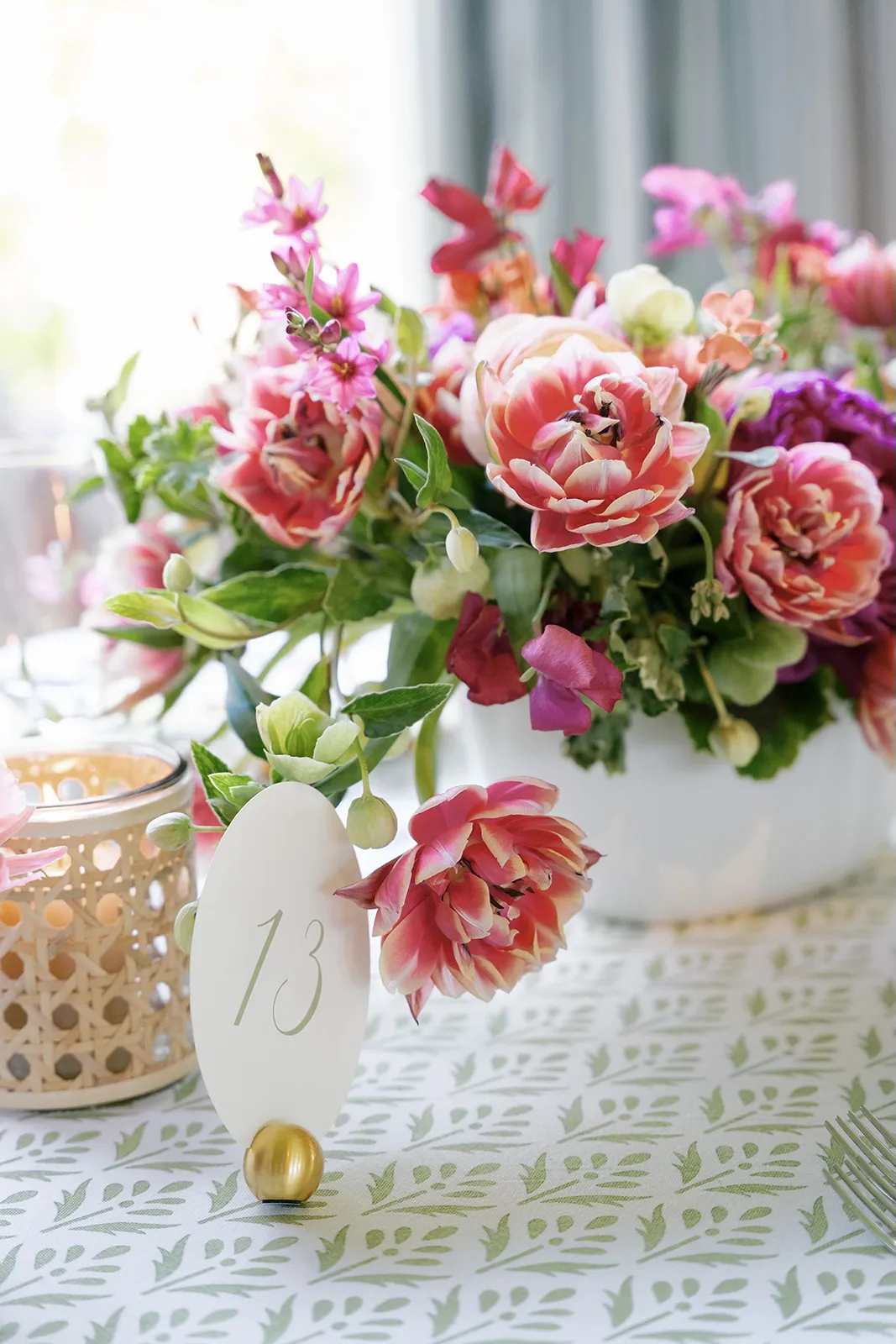 Close-up of a wedding table centerpiece featuring pink and coral florals, candles, and a numbered place card
