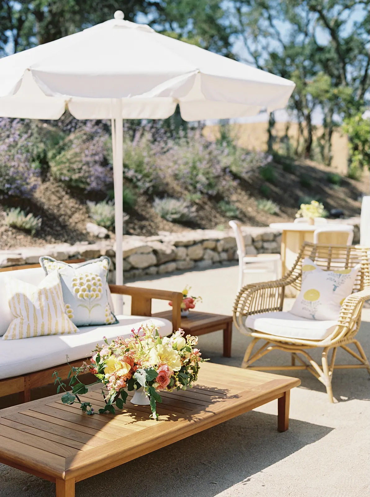 Outdoor lounge area with white umbrellas, wooden seating, and floral arrangements at a vineyard wedding reception