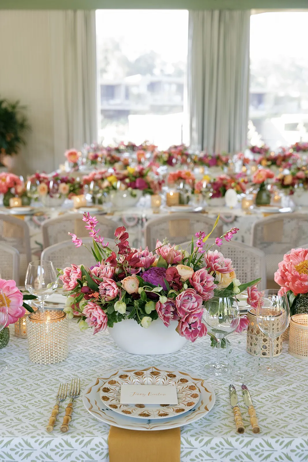 Elegant wedding reception table with pink floral centerpiece, patterned linens, and gold place settings