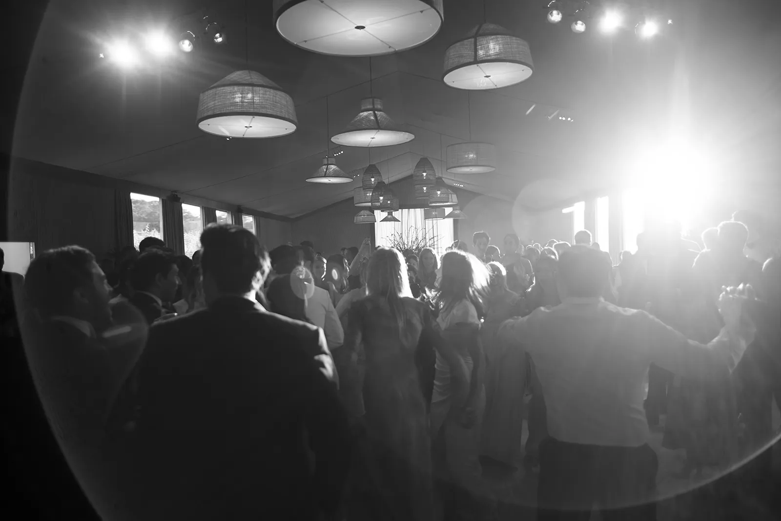 Wedding guests dancing together during a lively reception inside a tented space with hanging lantern lights