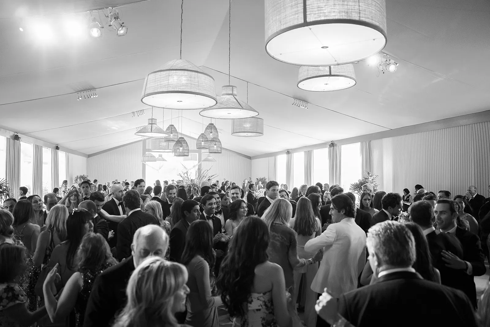 Lively wedding dance floor filled with guests dancing beneath woven pendant lights