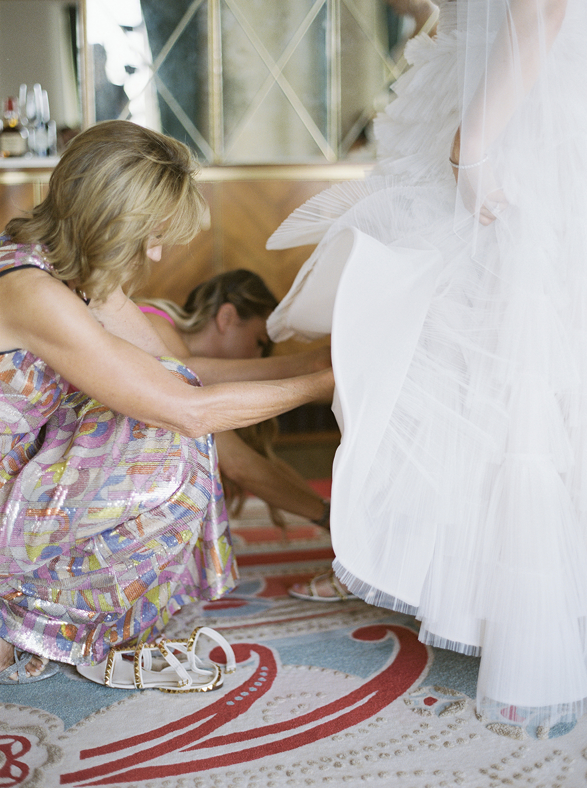 mother go the bride kneeling down assisting bride with shoes