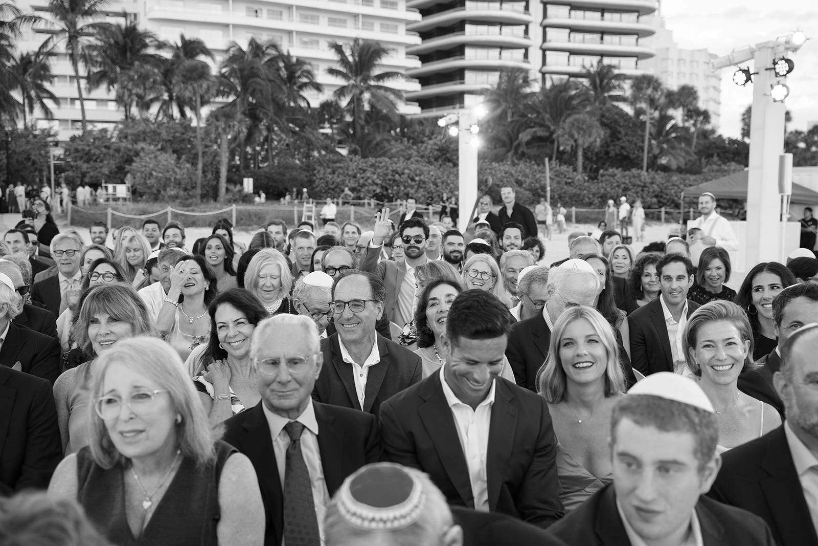 Wedding guests seated outdoors before the ceremony, smiling and chatting in black and white