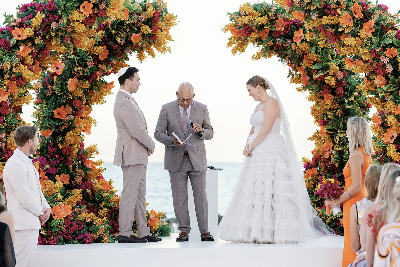 Bride and groom standing beneath colorful floral arches during an outdoor wedding ceremony