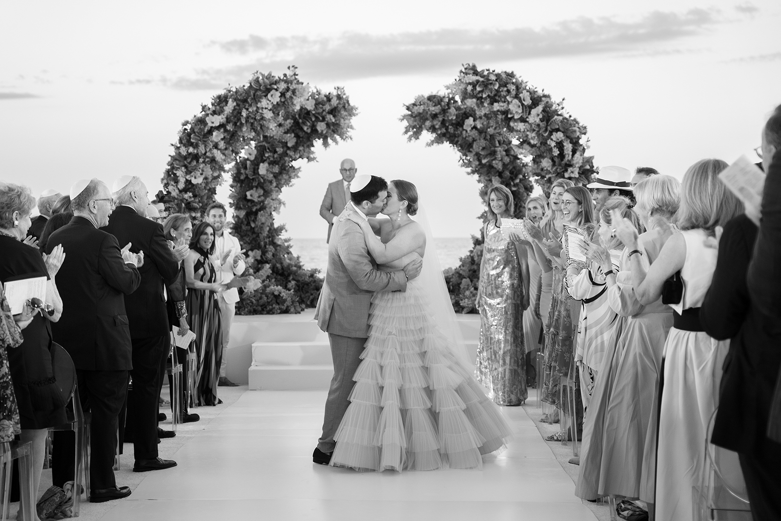 Bride and groom sharing their first kiss at the altar surrounded by cheering guests