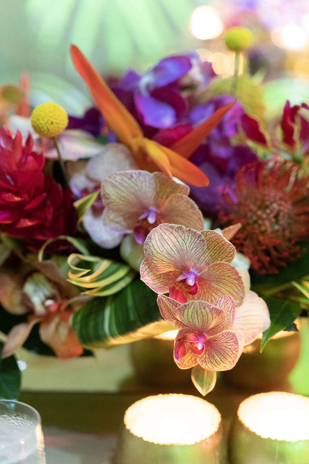 Close-up of a colorful tropical floral centerpiece with orchids and candles