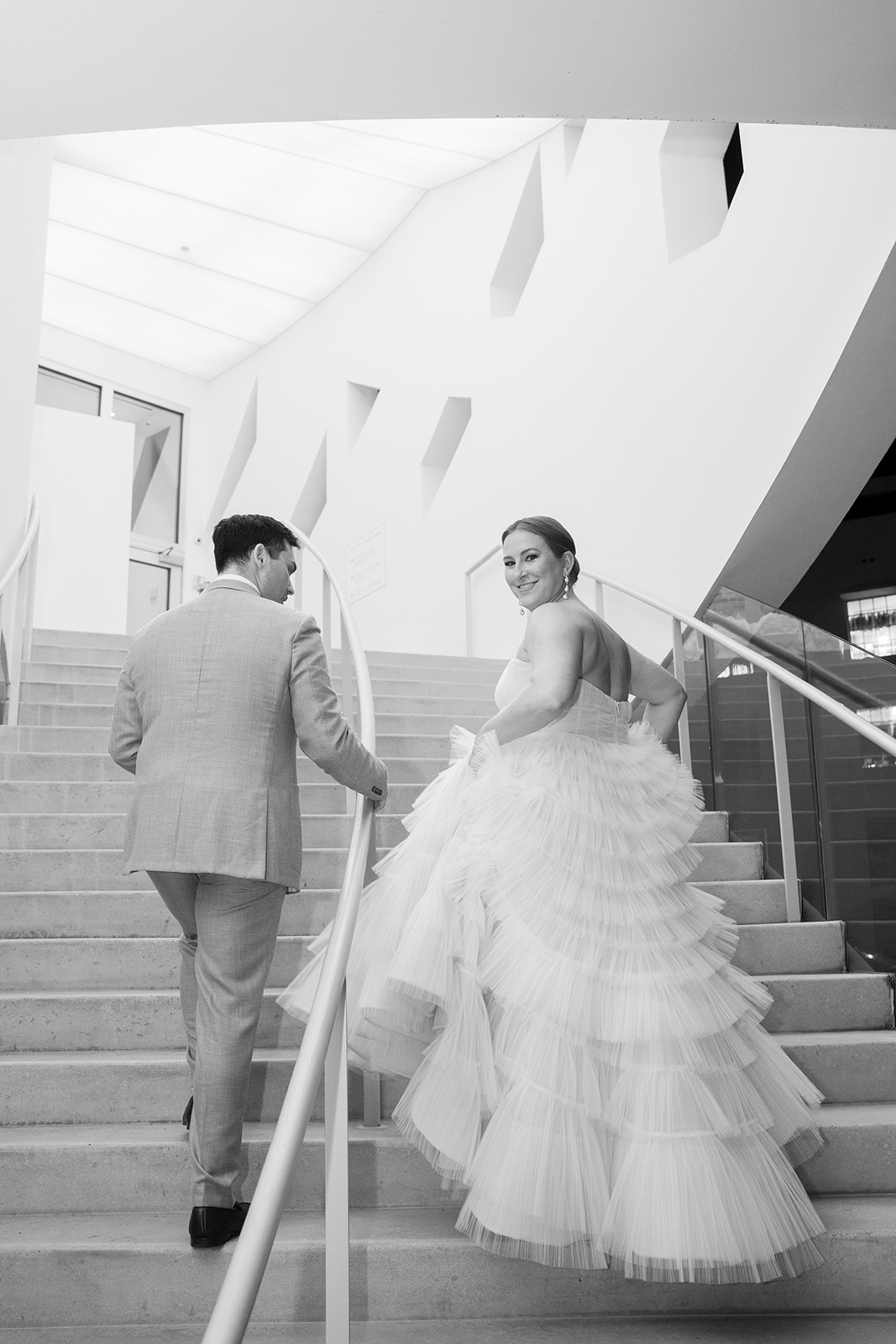 Bride looking back and smiling while walking up a modern staircase with the groom
