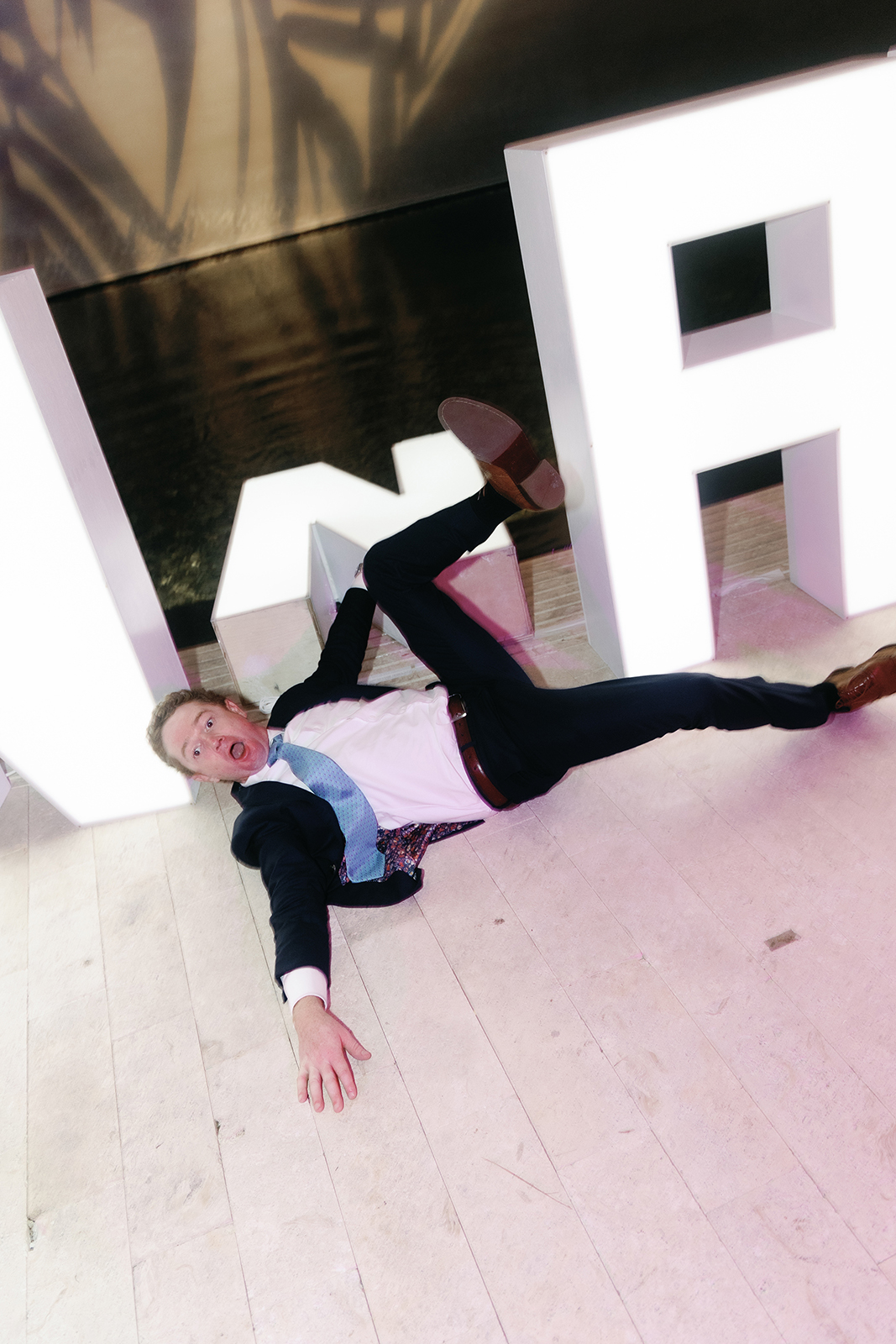 Wedding guest playfully lying on the floor in front of an illuminated sign during the reception