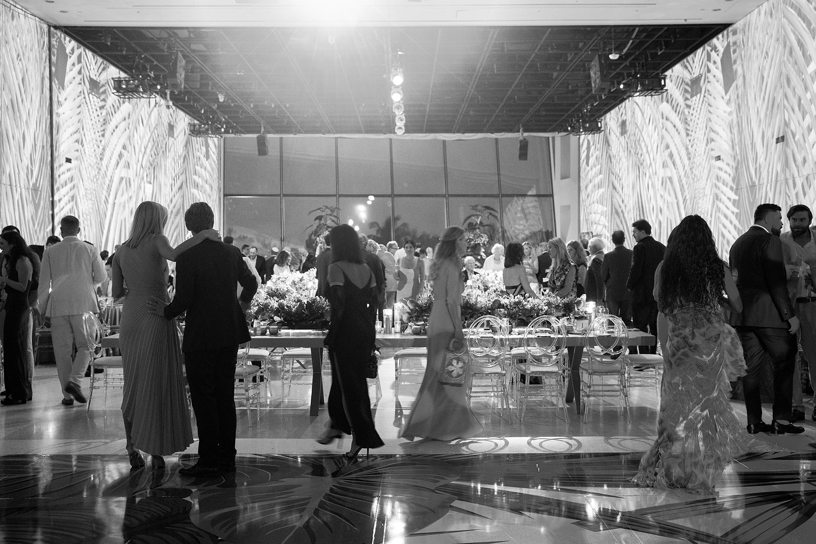 Wedding guests mingling around long reception tables filled with floral arrangements