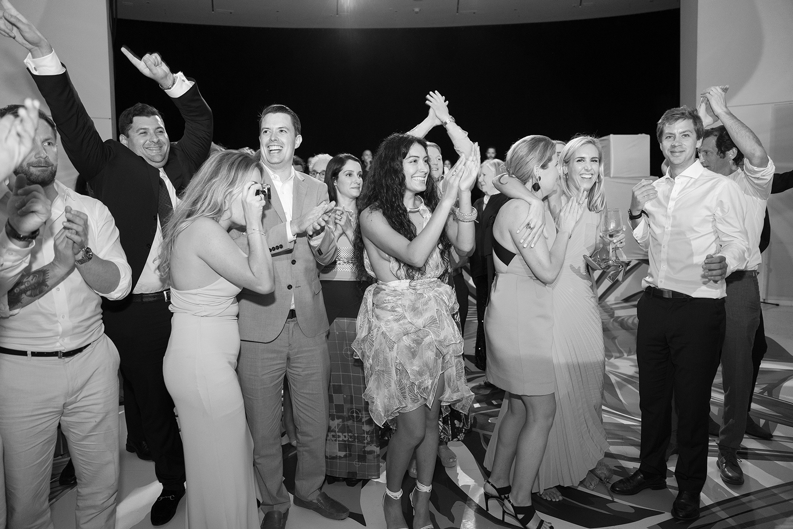 Black and white image of wedding guests cheering and applauding during reception festivities
