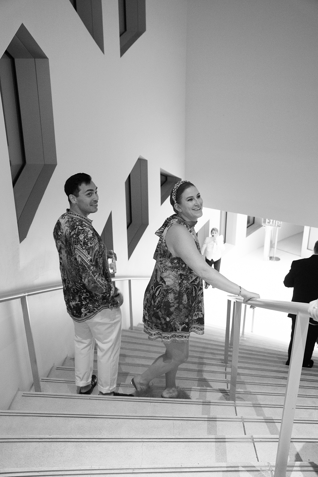 Black and white photo of a couple walking down a modern staircase together during their wedding celebration