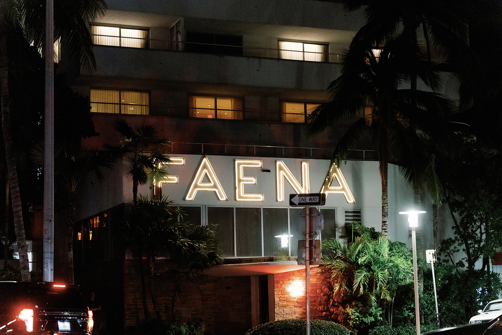 Night exterior of a luxury hotel entrance with illuminated FAENA sign, palm trees, and street lighting in Miami Beach