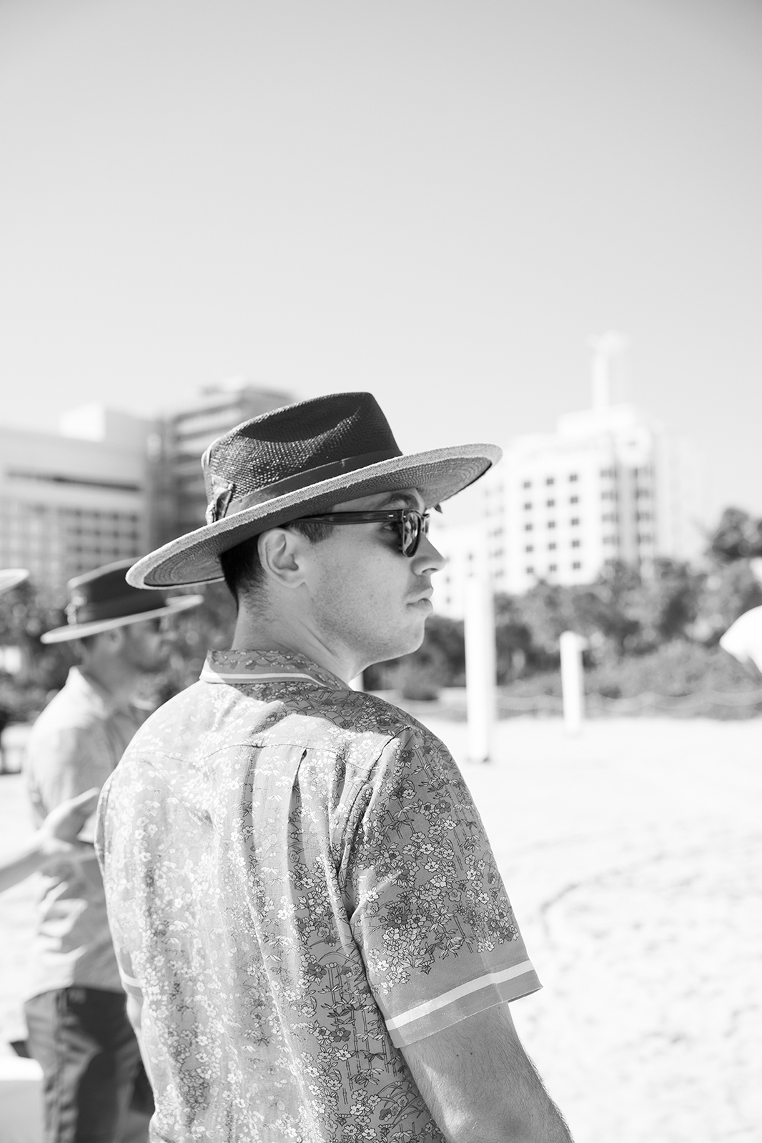 Groom wearing a straw hat looking toward the ocean at Faena Beach during a Miami wedding celebration