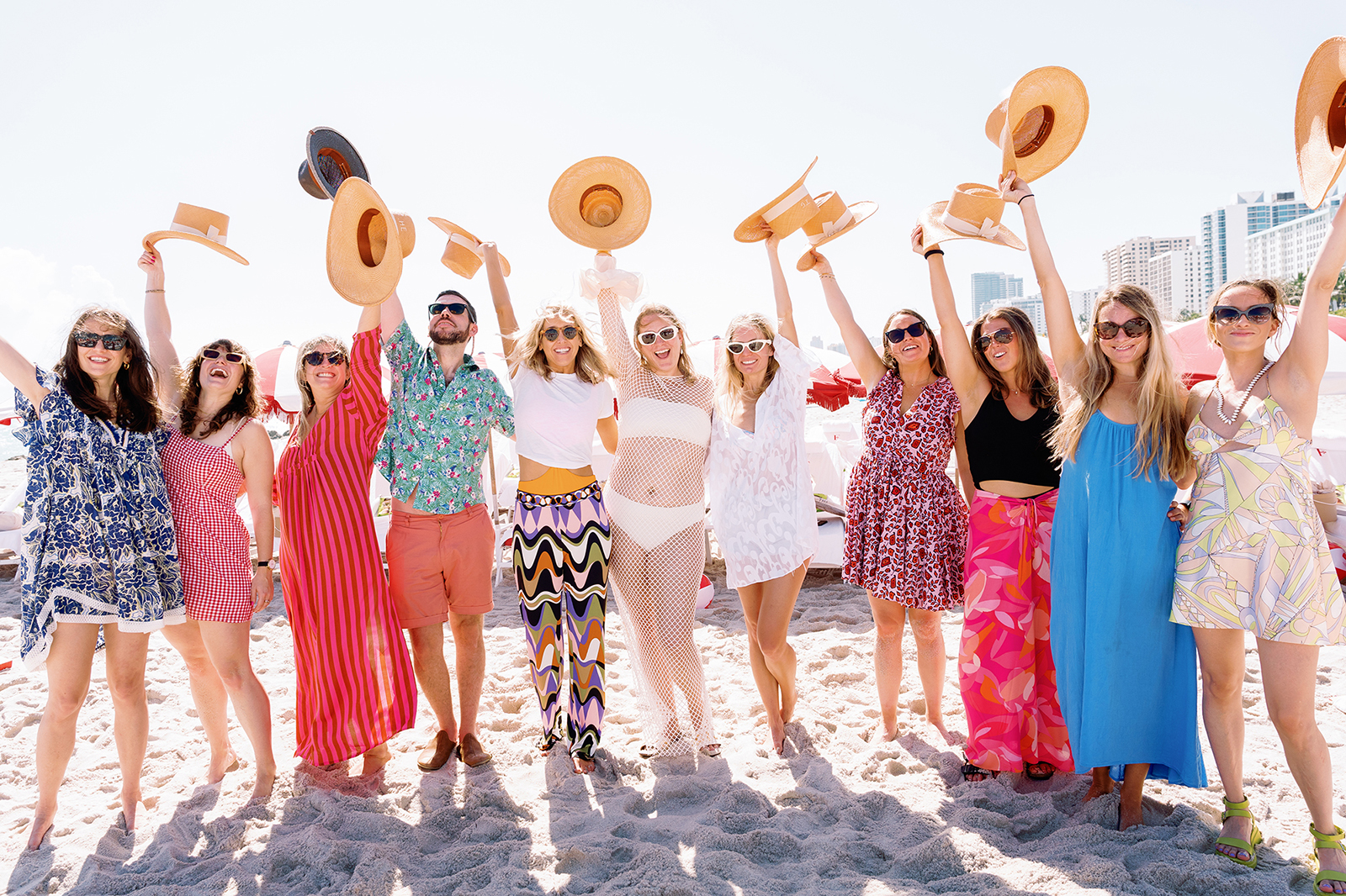Wedding guests throwing straw hats in the air during a fun beach wedding party