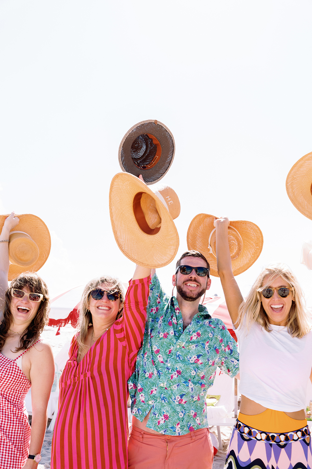 Wedding guests cheering with straw hats raised during a lively beach wedding weekend