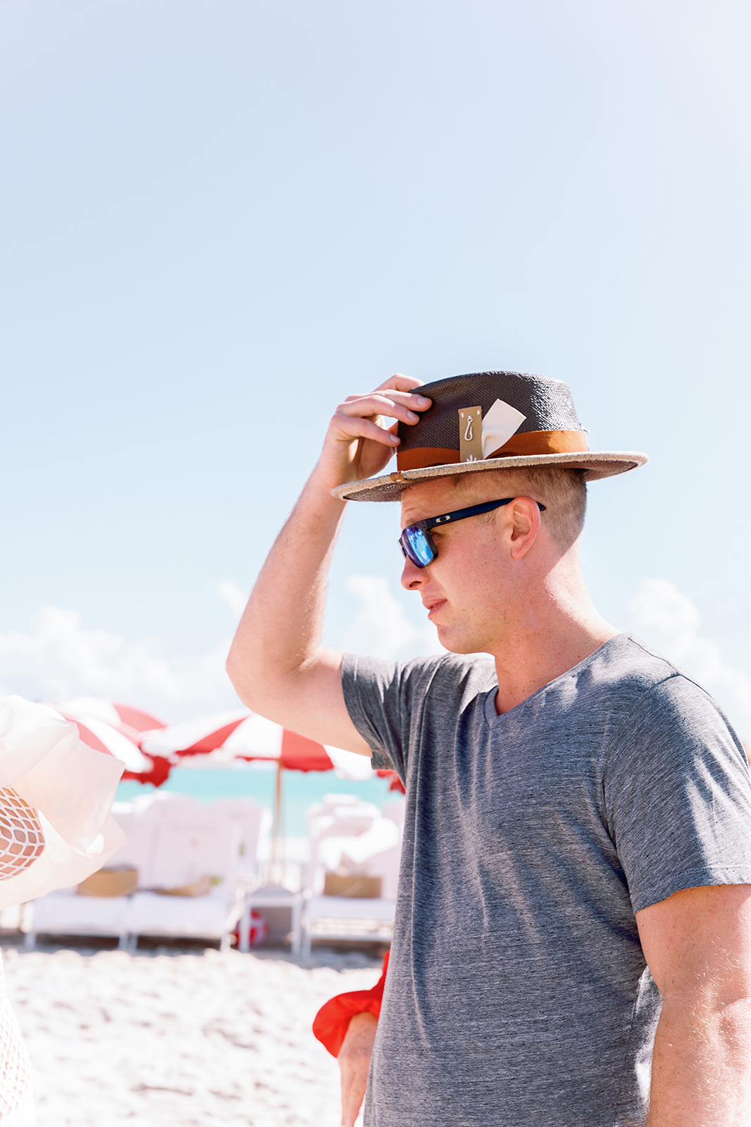 Wedding guest adjusting a straw hat during a sunny beach wedding celebration