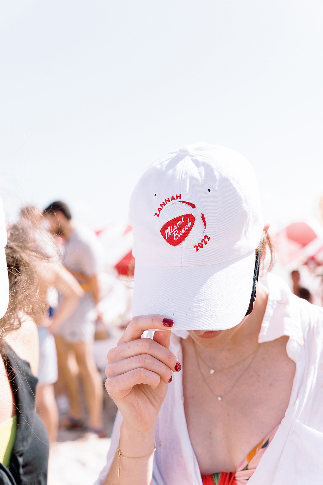 Close-up of a guest wearing a custom wedding baseball cap during a beach celebration