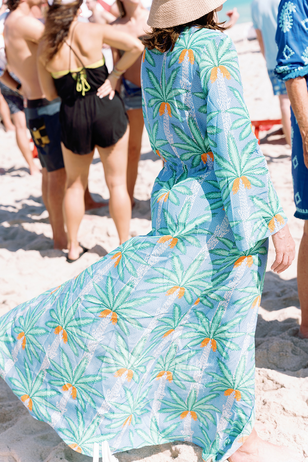 Wedding guest wearing a flowing patterned dress while walking across the sand at a beach celebration