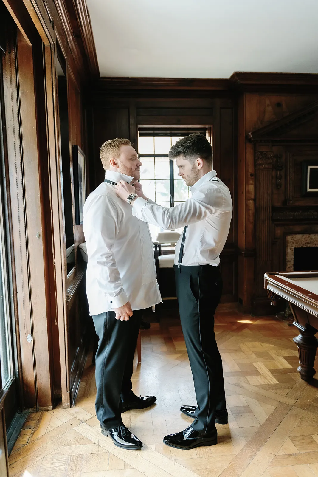 Groomsman helping the groom adjust his tie while getting ready for a Fisher Island wedding.