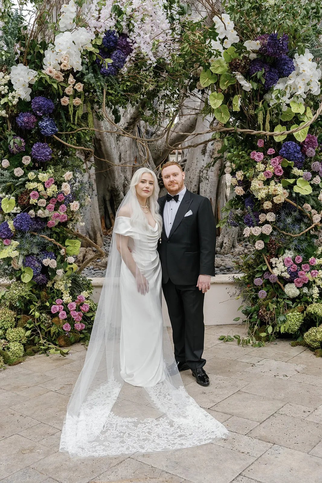Bride and groom standing beneath a lush floral arch at a Fisher Island wedding ceremony site