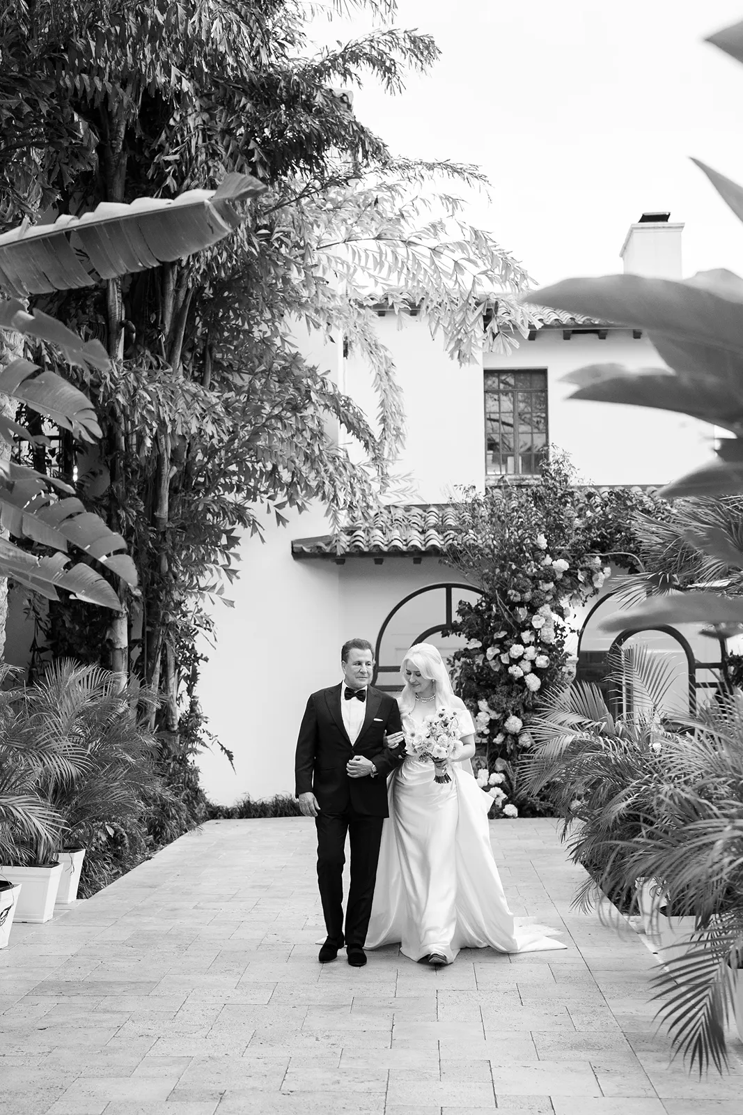 Bride walking with her father through a garden courtyard at a Fisher Island wedding ceremony