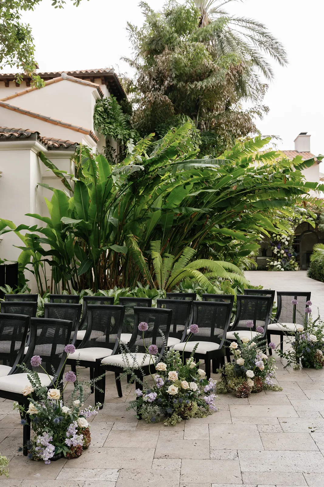 Fisher Island wedding ceremony setup with black chairs and floral aisle arrangements in a tropical courtyard